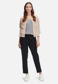 Lichtbeige colbert met twee voorzakken, gelaagd over een grijze top, gecombineerd met zwarte tapered broek en witte sportschoenen.