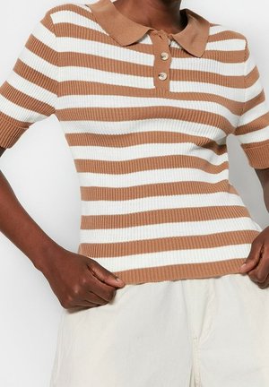 Persona que lleva una camiseta tipo polo de punto de manga corta a rayas marrones y blancas con dos botones, combinada con pantalones de color claro.
