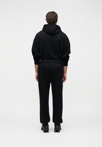 Μαύρο φούτερ με κουκούλα και αντίστοιχο παντελόνι φόρμας κατασκευασμένα από μαλακό ύφασμα, με άνετη εφαρμογή, ελαστική μέση και ελάχιστες λεπτομέρειες.