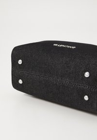 Pochette en denim noir avec quincaillerie en argent, présentant une finition texturée et des coutures visibles. Accentuée par trois clous en argent sur le fond.