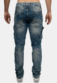 Pantaloni cargo in denim blu con molteplici tasche, lavaggio sbiadito e dettagli di cucitura in evidenza. Design a gamba affusolata con taglio dritto.