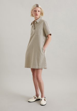 Gestreepte, kortärmelige kraagjurk in beige en wit, met een voorknopsluiting en zijzakken. Draagt met witte schoenen.