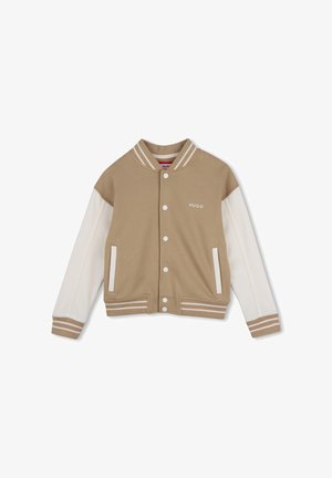 Veste universitaire beige et blanche avec boutons pression, col et poignets rayés, poches latérales, et logo "HUGO" sur la poitrine.