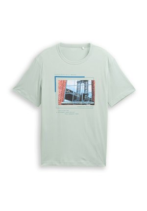 Jasnozielona koszulka z grafiką ceglanego budynku i metalowych mostów odbijających się w oknach, wraz z tekstem o widokach miejskich i kreatywności.