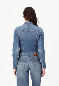 Giubbotto di jeans in blu chiaro con design aderente, chiusura a bottoni e due tasche posteriori. Presenta cuciture ricamate e una patch in pelle con logo.