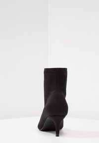 Černé kotníkové boty s elegantním designem, vyrobené z hladkého materiálu, s zúženým podpatkem a minimalistickým siluetou.