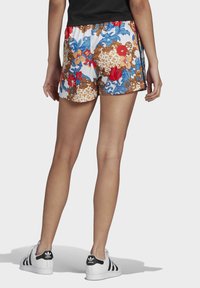 Shorts con estampado floral que presentan un vibrante rojo, azul y dorado sobre un fondo blanco, con una cintura elástica y un corte relajado.