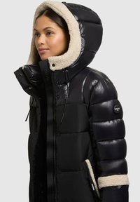 Fekete steppelt dzseki fényes felülettel, műszőrme béléses kapucnival. Cipzáras lezárással és logópáccal az ujján.