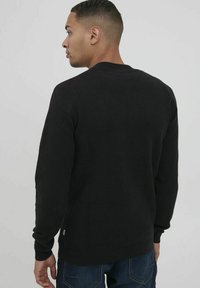 Svart stickad tröja med en texturerad design, rund halsringning och långa ärmar. Har ribbade muddar och nederkant för en figurnära look.
