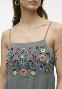 Grå klänning med tunna band som har intrikata blommönster i rött, gult, rosa och blått. Mjuk textur med en flödande silhuett.