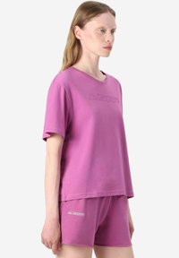 T-shirt in cotone rosa con maniche corte, caratterizzato da un dettaglio del logo in rilievo, abbinato a pantaloni corti coordinati che mostrano il logo, entrambi in una texture liscia.