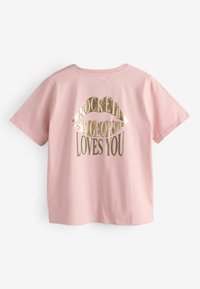 Rožinė medvilninė marškinėliai trumpomis rankovėmis su didele auksine lūpų grafika ir po ja esančiu tekstu „ROCKETT ST. GEORGE LOVES YOU“.