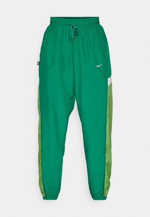 Pantalons de jogging athlétiques verts avec une texture douce, arborant un panneau latéral de couleur vert clair contrasté et un petit logo blanc à l'avant.