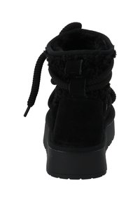 Black ankle boot featuring a soft, textured upper with a plush lining, secured by a round lace and accented with a looped pull tab. Flat platform sole.