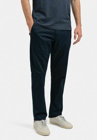 Marina blå, slim-fit byxor med en mjuk textur, sidofickor och en platt framtill, ihop med ljusa sneakers.
