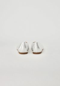 Ballerines argentées avec une finition métallique lisse, bout rond et semelle basse marron, présentant des coutures nettes et un design minimaliste.
