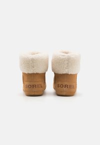 Stivaletti alla caviglia in suede color tovagliolo con un colletto in pelliccia sintetica bianca e soffice, con il marchio "SOREL" sul tallone e una silhouette liscia e arrotondata.