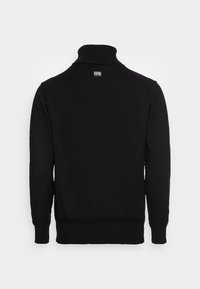 Pull en maille noire avec un col haut et des manches longues. Présente des bords-côtes aux poignets et à la taille. Étiquette visible au niveau de l'encolure arrière.