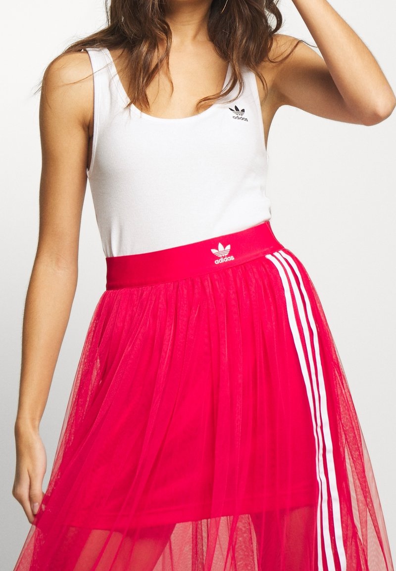 White tank top with black logo, paired with a pink tulle skirt featuring a wide waistband and three white vertical stripes.