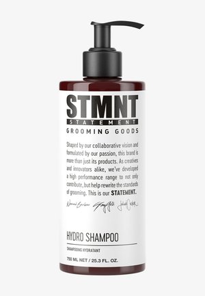 Dark amber plastic bottle with a black pump dispenser. White label featuring bold text and a detailed description. Contains 750 mL of hydro shampoo.