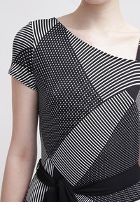 Svartvit klänning med blandade mönster: diagonala ränder, prickar och en omlottdesign, med en figursydd bodice och korta ärmar.