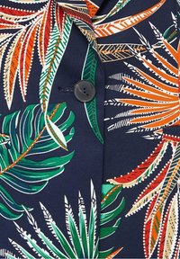 Tissu bleu foncé avec des motifs de feuilles tropicales en vert, orange et blanc, présentant un bouton noir et une boutonnière au centre.