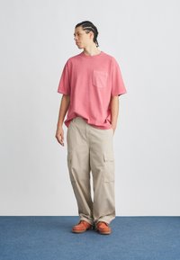 Ροζ βαμβακερό t-shirt με τσέπη στο στήθος, συνδυασμένο με μπεζ cargo παντελόνια με πλαϊνές τσέπες και πορτοκαλί παπούτσια με ανθεκτική σόλα.