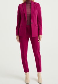Fuchsia skräddarsydd kostym med enblads blazer och rak benbyxa, bärs över en figursydd vinröd rullkrage, tillsammans med beige ankelstövlar.