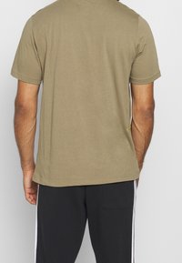 Oliven grøn kortærmet t-shirt i en blød bomuldsblanding med lige kant, der har enkel syning og en afslappet pasform set fra ryggen.
