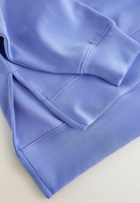 Lyse lilla sweatshirt med glat tekstur. Har ribbede ærmeafslutninger og en syet kant. Lagdelt design med synlige sømme og blødt stof.