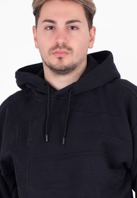 Czarna bluza z kapturem o teksturowanym wzorze, z kapturem ze ściągaczem i poziomymi przeszyciami. Wykonana z miękkiej tkaniny z mieszanki bawełny.