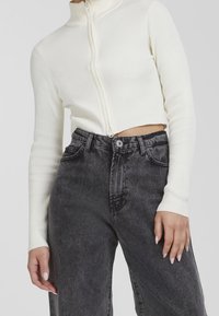 Vit rippad cropped zip-up topp i kombination med högmidjade svarta jeans, som har en urtvättad struktur och klassisk femficksdesign.