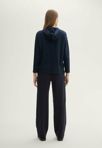 Felpa con cappuccio blu navy a maniche lunghe, realizzata in un tessuto morbido e testurizzato. Abbinata a pantaloni scuri a gamba larga per una silhouette rilassata.