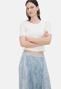 Valge volangiga lühikeste varrukatega crop top, mille juurde on sobitatud helesinine volditud seelik, millel on peen, tekstuurne muster. Kuldse ringehelega kõrvarõngad.