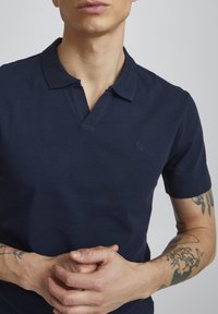 Marineblå polo-skjorte, korte ermer, kragehals med V-splitt, myk tekstur, subtil logo-detalj på venstre bryst.