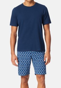 Mørkeblå t-shirt med korte ærmer, parret med blå mønstrede shorts med firkanter og rektangler i forskellige nuancer af blå og hvid.