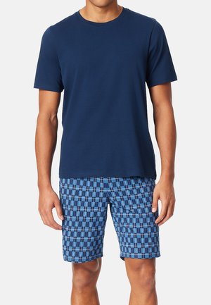 Marinefarbenes T-Shirt mit kurzen Ärmeln, kombiniert mit blauen gemusterten Shorts, die Quadrate und Rechtecke in verschiedenen Blau- und Weißtönen zeigen.