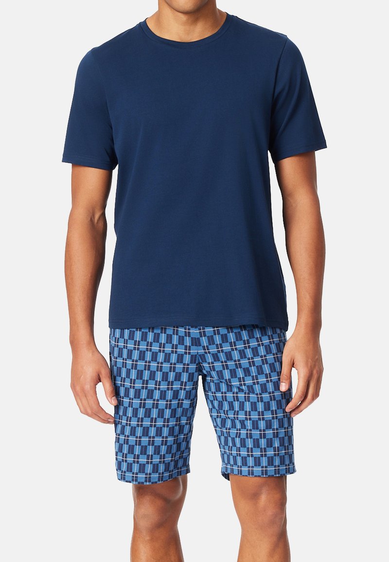 Mørkeblå t-shirt med korte ærmer, parret med blå mønstrede shorts med firkanter og rektangler i forskellige nuancer af blå og hvid.