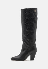Black knee-high boots made of textured leather, featuring a pointed toe and a block heel, with a small gold logo on the upper side.