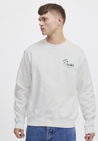 Hvit bomullssweatshirt med lange ermer, med et grønt grafisk design på brystet, ribbestrikkede mansjetter og rund hals.