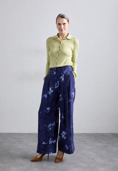 Light green ribbed cardigan with a collar, paired with wide-leg navy trousers featuring a floral pattern. Brown pointed high heels.