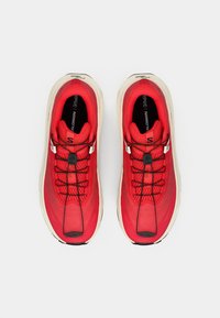 Κόκκινα αθλητικά παπούτσια με υφασμάτινο επάνω μέρος με υφή, μαύρα ελαστικά κορδόνια, λευκή σόλα και παχύ, μαλακό σχέδιο. Ορατά λογότυπα στα πλάγια.