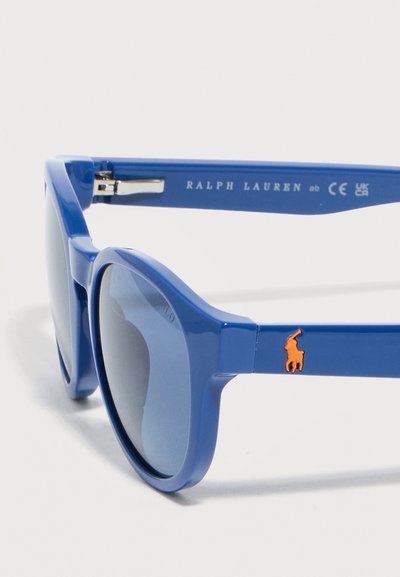 Niebieskie okulary przeciwsłoneczne Ralph Lauren z prostokątnymi oprawkami, ciemnymi soczewkami i pomarańczowym logo polo na zauszniku.