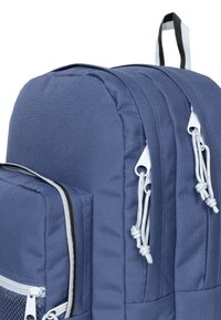 Zaino in tessuto blu con parte superiore arrotondata, scomparti con zip, accenti grigi e spallacci regolabili. Presenta una superficie esterna testurizzata e linguette di facile presa.