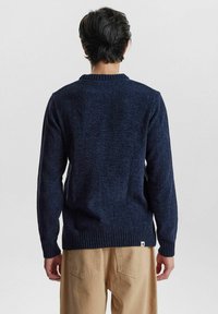 Dunkelblauer Strickpullover mit geripptem Rundhalsausschnitt und Bündchen; hat eine strukturierte Oberfläche und wird mit beigen Hosen kombiniert.