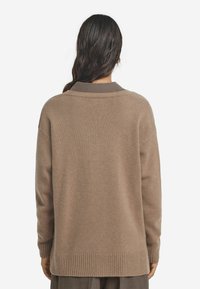 Beiger, übergroßer Pullover mit geripptem Saum und Bündchen. Hat ein schlichtes Design und einen braunen Kragen. Hergestellt aus einem weichen, strukturierten Material.
