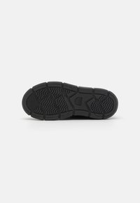 Semelle de sneaker en caoutchouc noir avec un motif de semelle texturé, présentant des rainures profondes et des éléments de design circulaires pour une meilleure adhérence et traction.