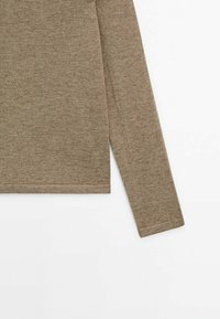 Manche de chemise en tissu tricoté marron à manches longues et section inférieure du torse sur fond blanc.