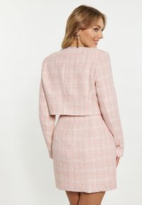 Rochie roz din tweed cu o jachetă scurtă structurată, având un model cu carouri, mâneci lungi și un finisaj texturat.