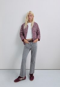 Chaqueta floral acolchada en tonos rosa y morado, camiseta corta blanca, jeans de pierna ancha grises y zapatillas burdeos con acentos blancos.